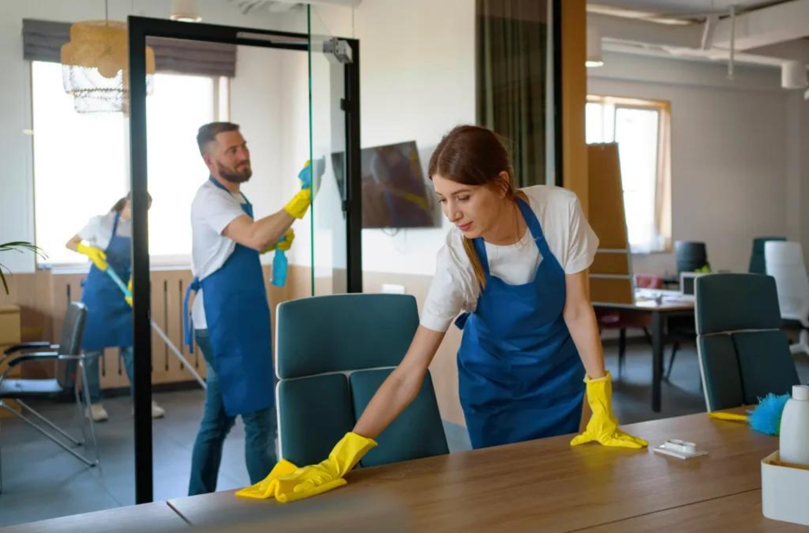 Cleaning professionals maintaining desks and glass in a bright office.